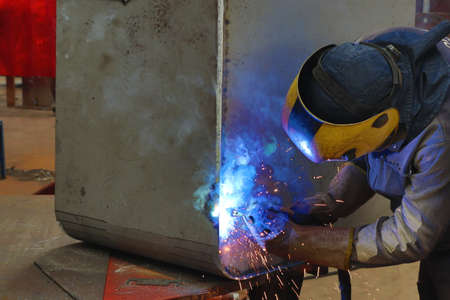 Welder at work in a factory welding metal with sparks and smoke