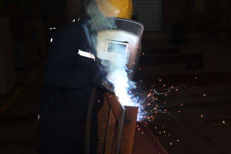 Welder at work in a factory. The welder welds metal with sparks.