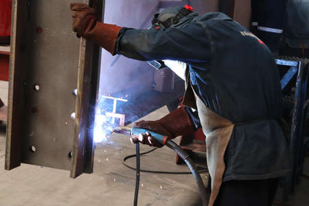 Welder working with arc welding machine to weld steel at factory.
