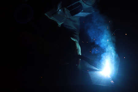Welder working with arc welding machine to weld steel at factory.
