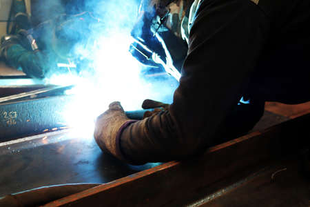 A welder welds a metal structure with a welding torch.