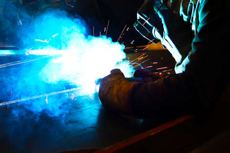 Welding of metal structures by electric arc welding machine. Worker in protective clothing welds...