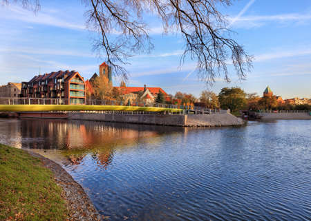 Modern metal bridge over Oder river on Tumski Island and St. Elizabeth's Church tower on background,...