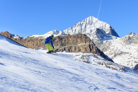 Male snowboarder on the slope with high mountain peaks on backgroundの写真素材