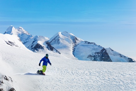 Male snowboarder on the slope with mountain peaks on backgroundの写真素材