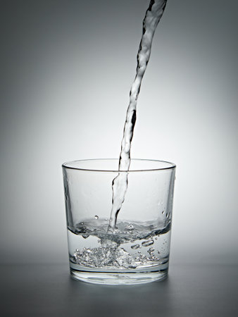 Pouring water into a glass on gray background. Shallow depth of fieldの写真素材