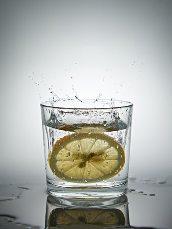 lemon splashing into a glass of water on a gray backgroundの写真素材