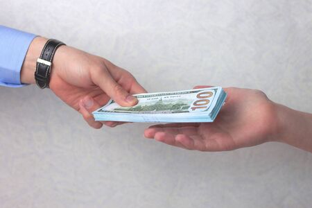 A man's hand with a watch gives a wad of money to a woman