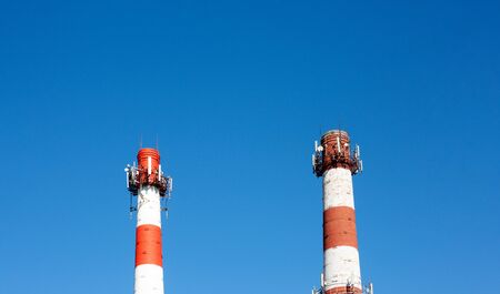 Two tall pipes are painted in white and red stripes with multiple antennas at the top against the blue skyの写真素材