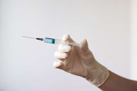 A rubber gloved hand holds a syringe with a needle filled with a blue liquid.の写真素材