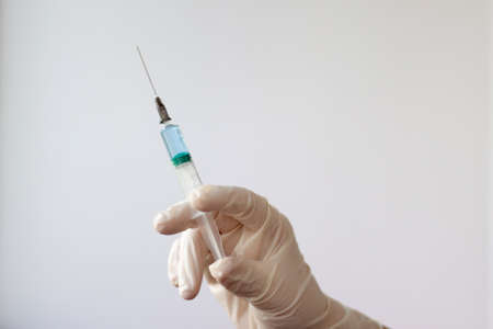 A rubber gloved hand holds a syringe filled with a blue liquid needle up.の写真素材
