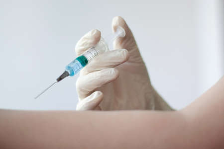 A rubber gloved hand holds a syringe filled with a blue liquid and gives an injection to the other hand.の写真素材
