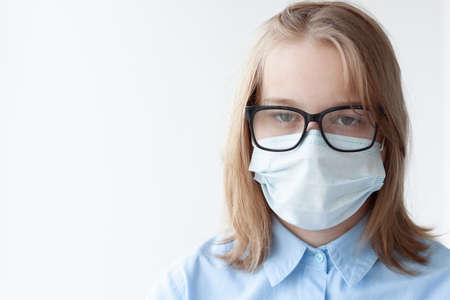 A teenage girl, blonde, in a blue shirt, a medical mask and glasses on a white background.の写真素材