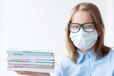 A teenage girl, blonde, in a blue shirt, wearing a medical mask and glasses on a white background,...
