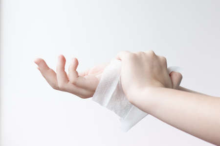 One hand wipes the other hand with a damp antibacterial cloth on a light backgroundの写真素材