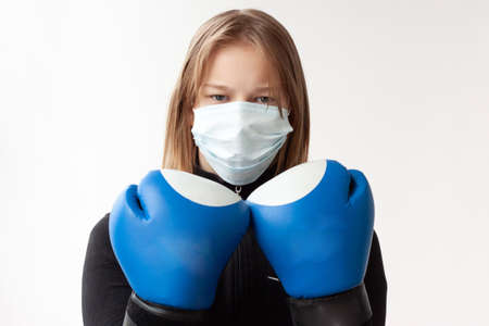 A girl with blond hair in a medical mask and blue Boxing gloves stands in a boxer's pose, hands near her face.の写真素材