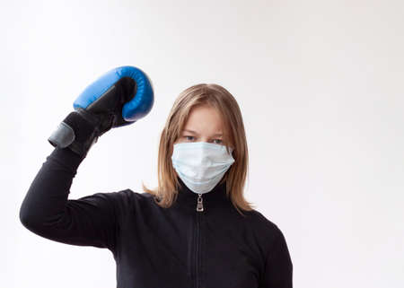 A girl with blond hair in a medical mask and blue Boxing gloves stands in a boxer's pose, right hand raised up, she is the winner.の写真素材