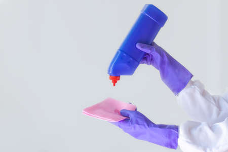 Two hands in purple rubber gloves, one holding a pink cloth for cleaning the surface, the other a blue bottle of cleaning agent. Concept of cleanliness, cleaning, new reality, surface treatmentの写真素材