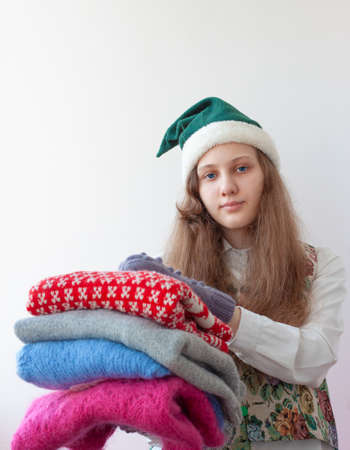 A girl in an elf hat holds several knitted Christmas sweaters in her hands.の写真素材