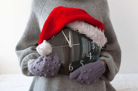 Hands in mittens are holding the clock on which the Santa Claus hat is wornの写真素材
