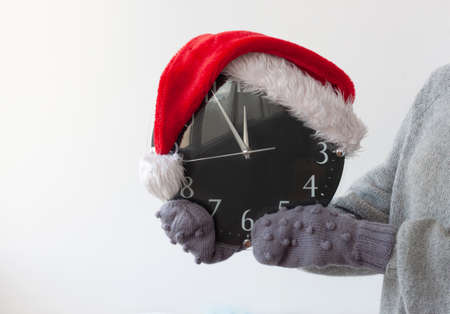 Hands in mittens are holding the clock on which the Santa Claus hat is wornの写真素材