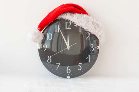A clock in a Santa Claus hat on a white background shows five minutes to twelveの写真素材