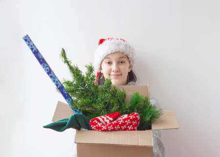 A teenage girl holds out a box with an artificial Christmas tree, a Christmas sweater and a roll of wrapping paperの写真素材
