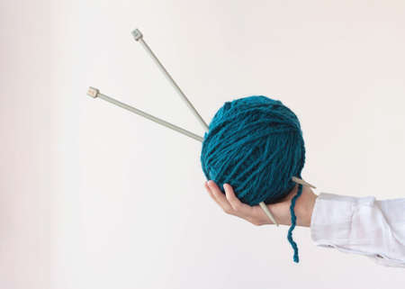 One hand holds a large ball of yarn and knitting needles