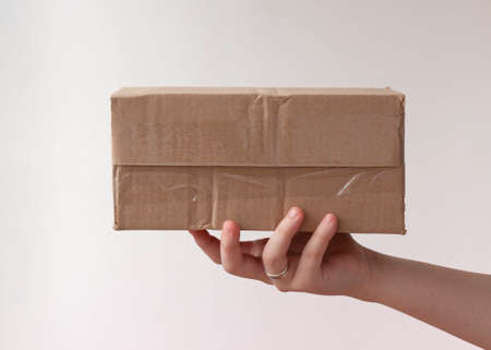 A hand holds out a package, a crumpled cardboard boxの写真素材