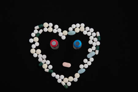 A heart of pills and two bottles of vaccine on a black background