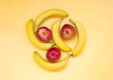 Five bananas and three red apples lie on a yellow backgroundの写真素材