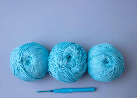 Three balls of blue cotton yarn lie on a blue background next to a knitting hook top viewの写真素材