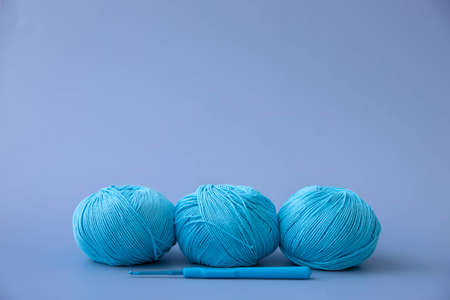 Three balls of blue cotton yarn lie on a blue background next to a knitting hook side viewの写真素材