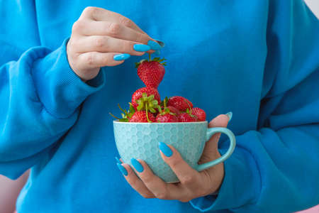 One hand holds a yellow bowl with strawberries the other holds one berry by the stemの写真素材