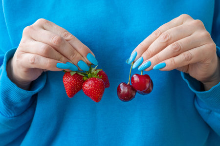 There are three strawberries in one hand and cherries in the otherの写真素材
