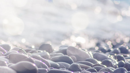 Sea pebble stones and water, defocused sun lights bokeh nature background. Natural beach stones background, wallpaper soft focus.の写真素材