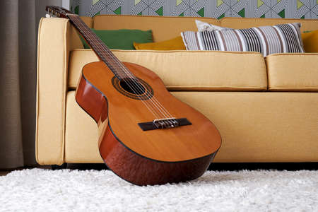 Classic guitar on the carpet close to the soft elegant yellow sofa. Musical instruments in interior...