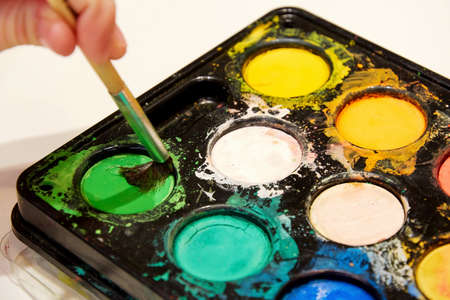 Hand with a brush draws with paints from the palette. Artistic and hobby backgroundsの写真素材