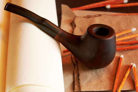Smoking pipe with matches and burnt letter and old scrolls. Atmospheric vintage desk