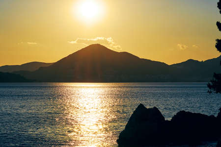 Bright sun and sunset lights over the mountain peak on the sea coast. Sun Path reflection in the waterの写真素材