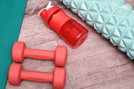 Womens fitness stuff on the wooden floor in the sports gym. Bottle, dumbbell, roller and other...