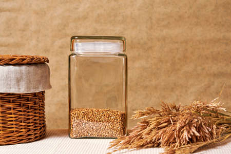 Raw buckwheat, ears of wheat and a basket on the rural kitchen table. Traditional food and cookingの写真素材