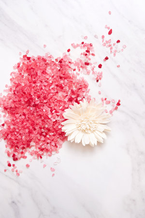 Pink bath salt scattered on the marble table in spa salon with flowers. Healthcare and alternative medicineの写真素材