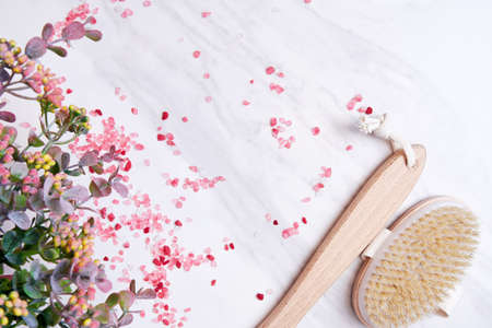 Wooden scrub brush, scented sea salt, flowers and herbs on the marble table. Spa salon backgrounds...