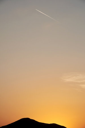 Vertical image with airplane high in the sky over the mountain silhouette. Transportation and travel...