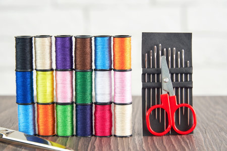 Rows of spools of colorful sewing threads and sew scissors on the table. Sewing production, hobby...