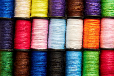 Background pattern of set of colorful rainbow sew thread spools on the wooden tailor table....