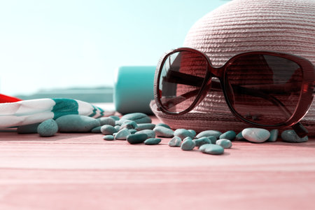 Straw hat, cream bottle, sunglasses and pebbles on the wooden table on terrace. Seaside and travel accessoriesの写真素材
