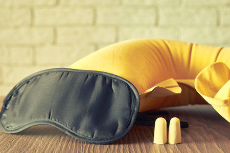 Travel sleep equipment on the wooden table. Relax in the trip. Face blind mask, inflatable pillow and earplugsの写真素材