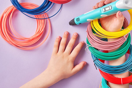 Kids hand with a new 3D pen and a bunch of plastic rings playing on the table. Hobby, toys and craft backgrounds. Banner with copy space for textの写真素材